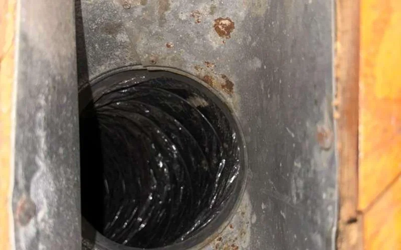 Rust-stained sheet-metal plenum with a duct takeoff — a common leak point