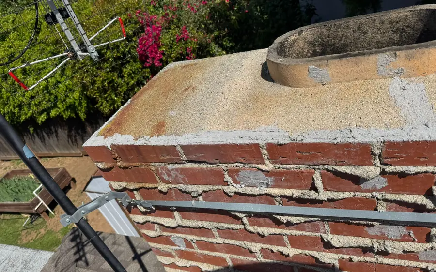 A corroded chimney cap and cracked crown on a coastal rooftop, staged for repair